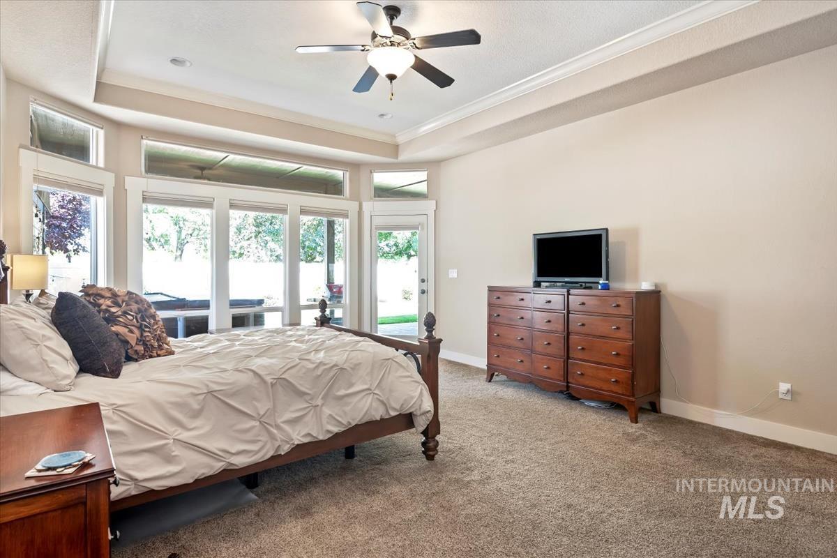Carpeted bedroom featuring a tray ceiling, access to exterior, a ceiling fan, and ornamental molding