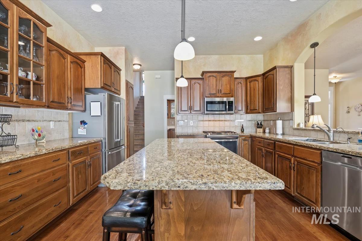 Kitchen featuring a kitchen bar, hanging light fixtures, brown cabinetry, light stone countertops, and a textured ceiling