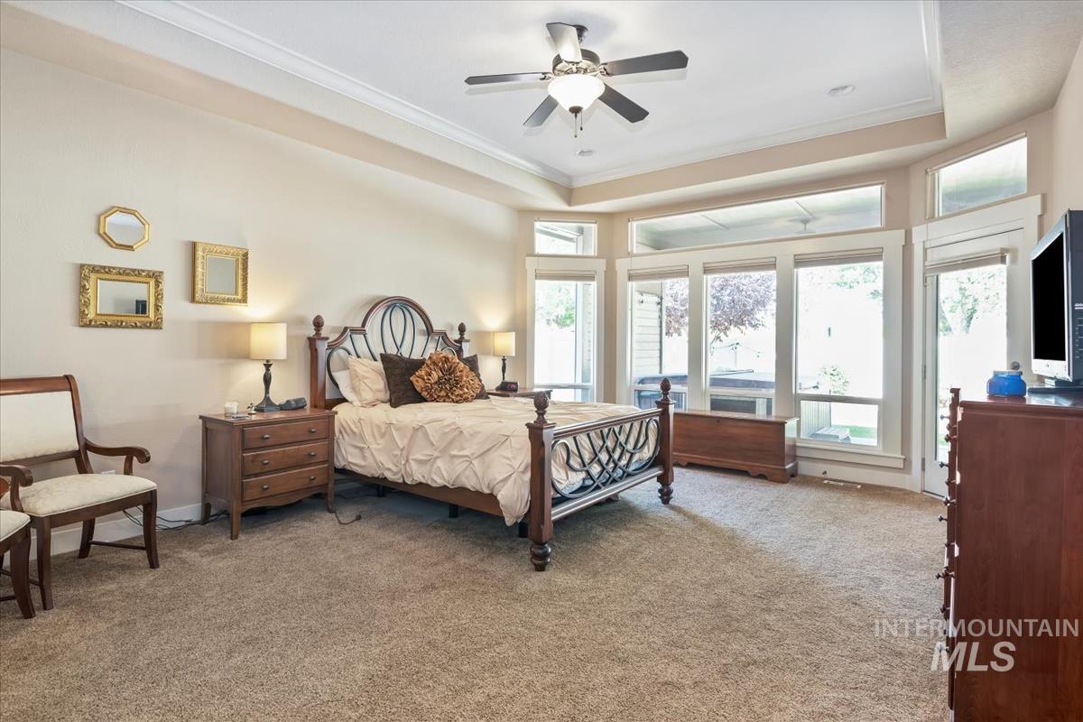 Bedroom featuring light colored carpet, a raised ceiling, crown molding, ceiling fan, and access to outside