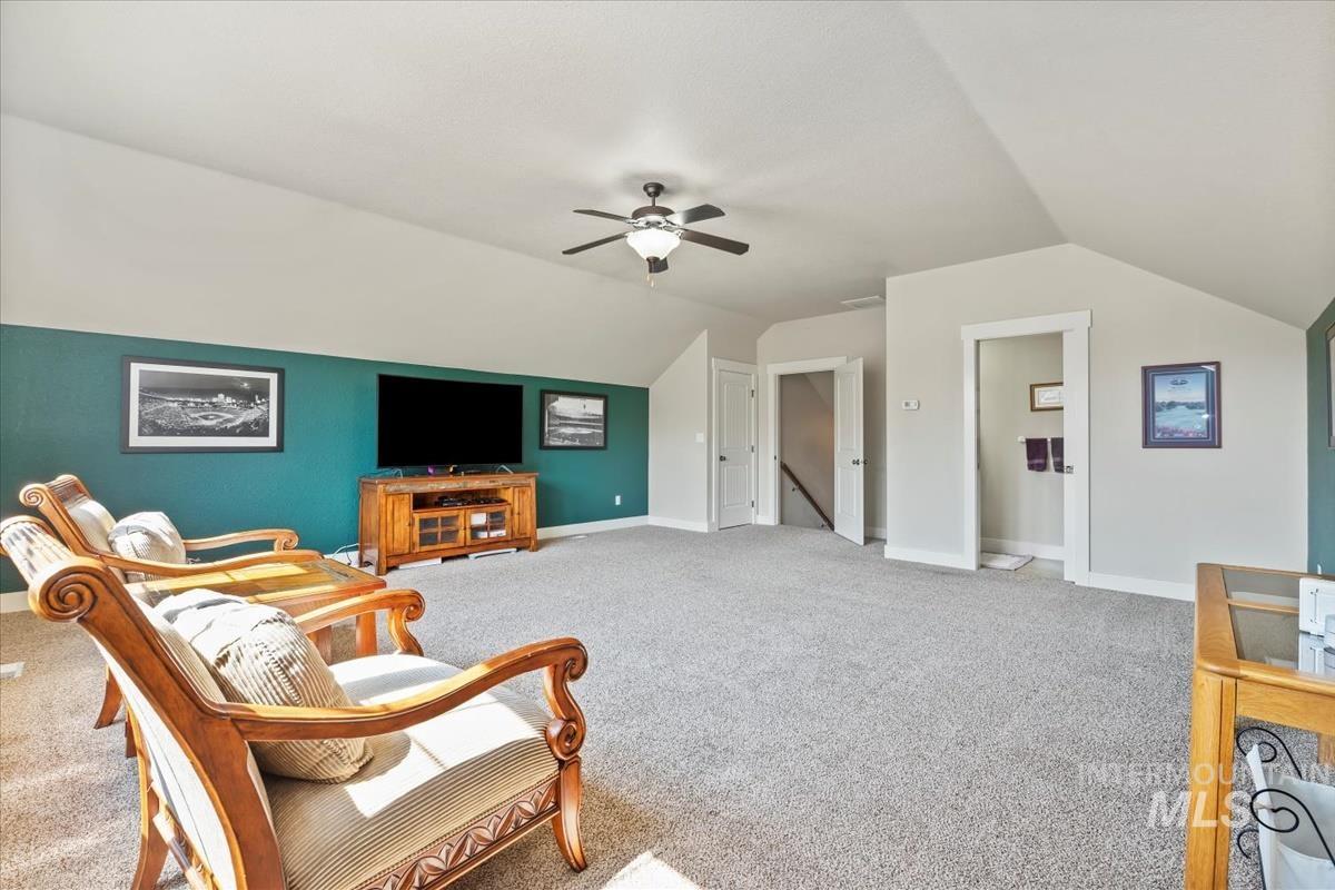 Living area featuring an upstairs landing, vaulted ceiling, light carpet, and a ceiling fan