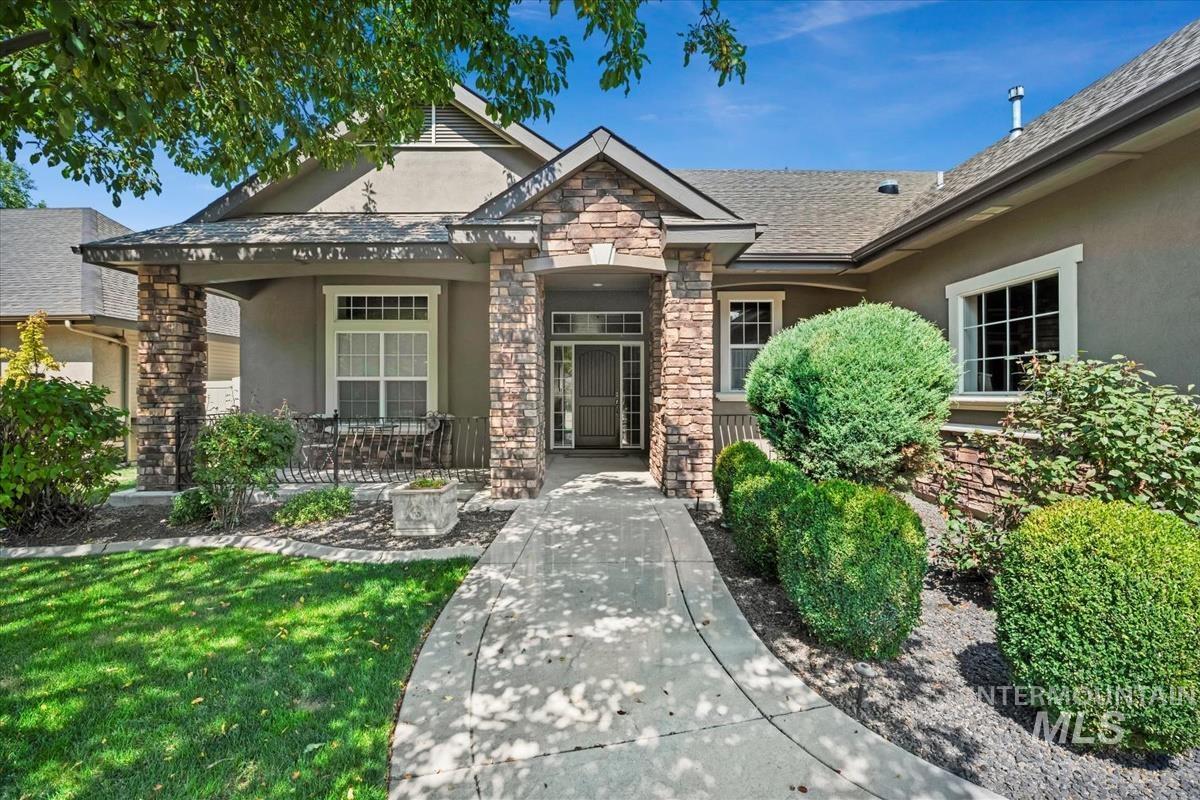 View of exterior entry featuring stucco siding, stone siding, a yard, and covered porch