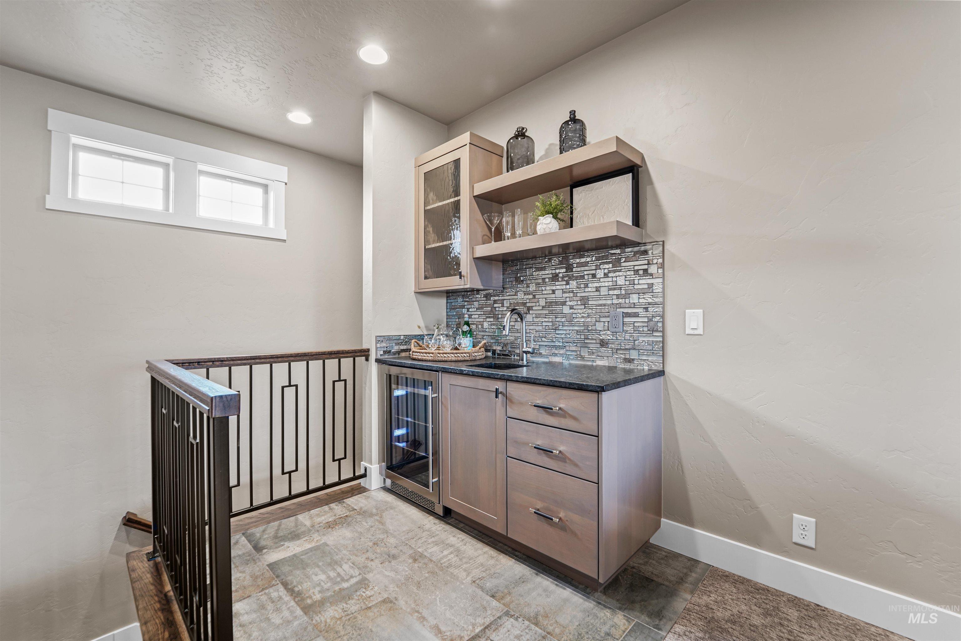 Indoor wet bar featuring decorative backsplash, open shelves, dark stone counters, wine cooler, and glass insert cabinets