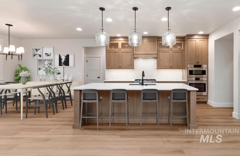 Kitchen featuring light countertops, brown cabinets, a center island with sink, light wood-style floors, and recessed lighting
