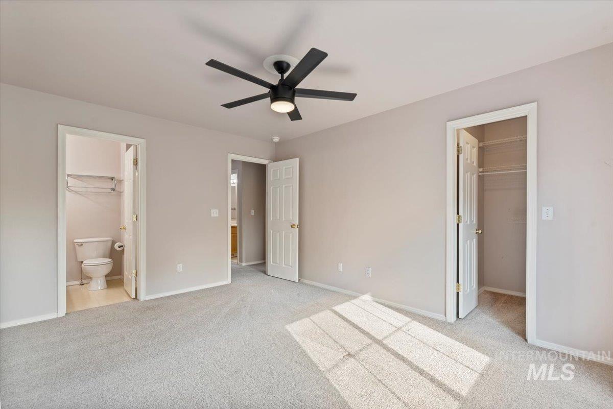 Unfurnished bedroom with light colored carpet, a spacious closet, ceiling fan, and connected bathroom