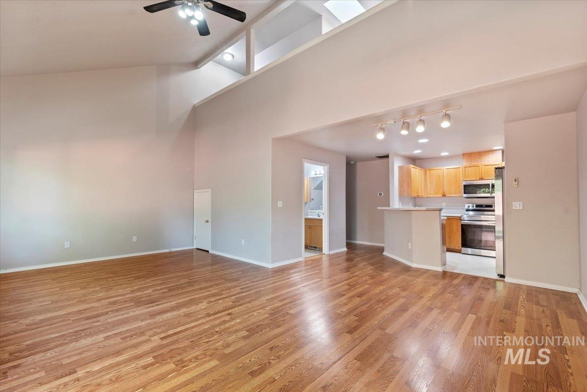 Unfurnished living room with light wood-style flooring, a high ceiling, ceiling fan, and track lighting