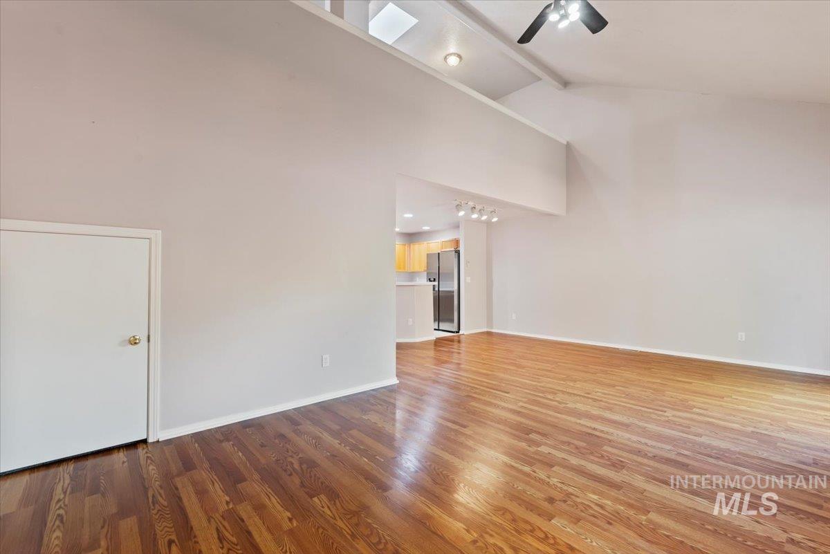 Unfurnished living room with beamed ceiling, light wood-style floors, a ceiling fan, and high vaulted ceiling