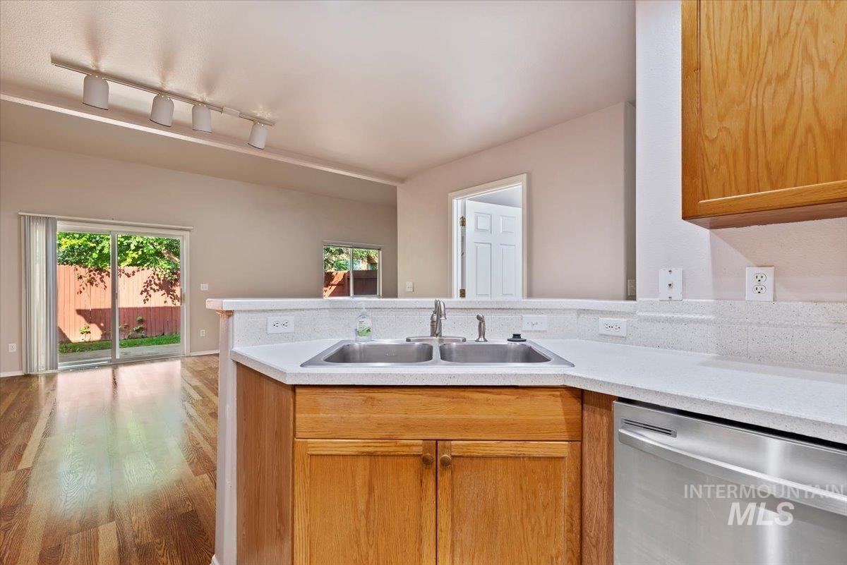 Kitchen featuring stainless steel dishwasher, light countertops, rail lighting, and a peninsula