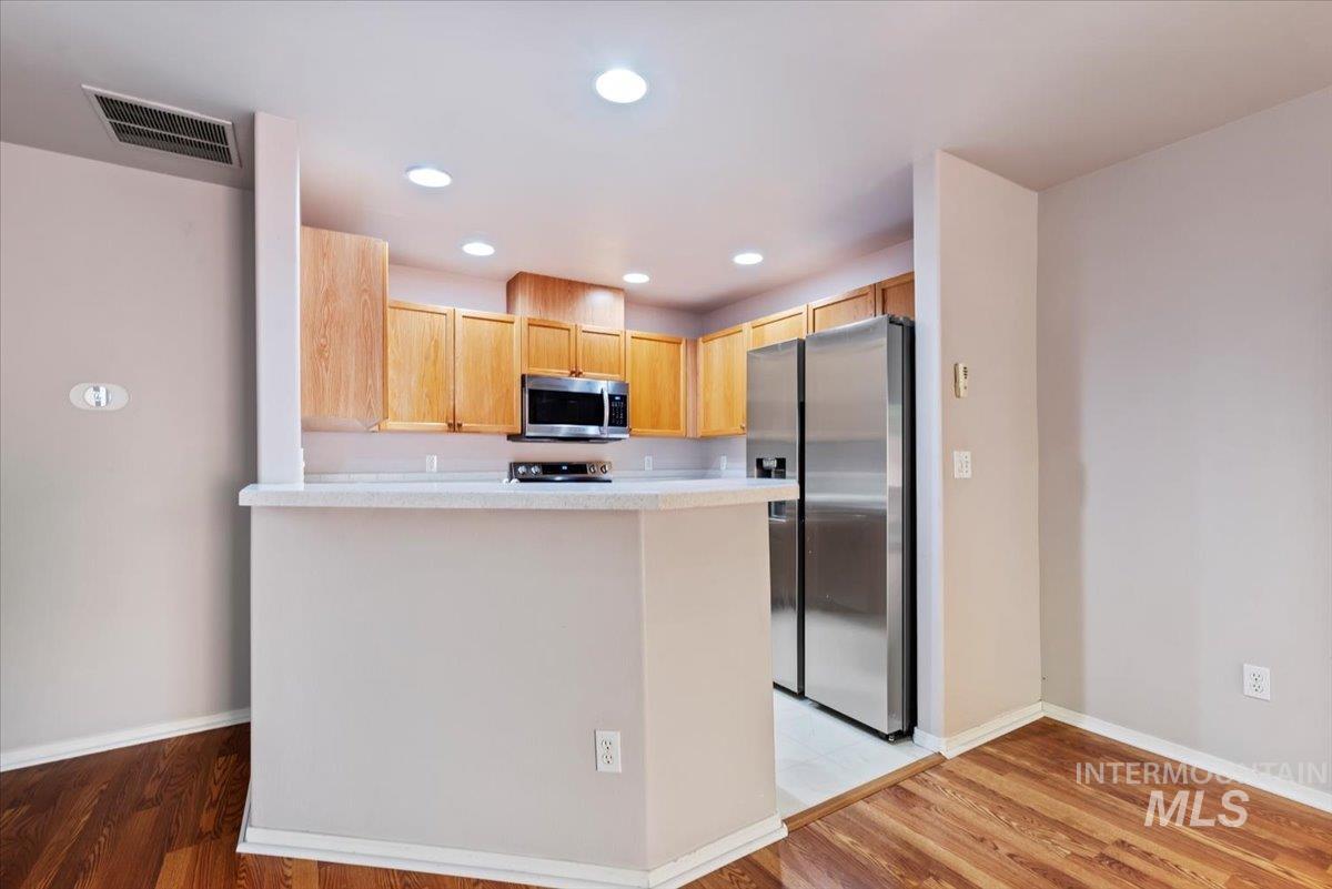 Kitchen featuring appliances with stainless steel finishes, light wood-type flooring, a peninsula, recessed lighting, and light brown cabinets