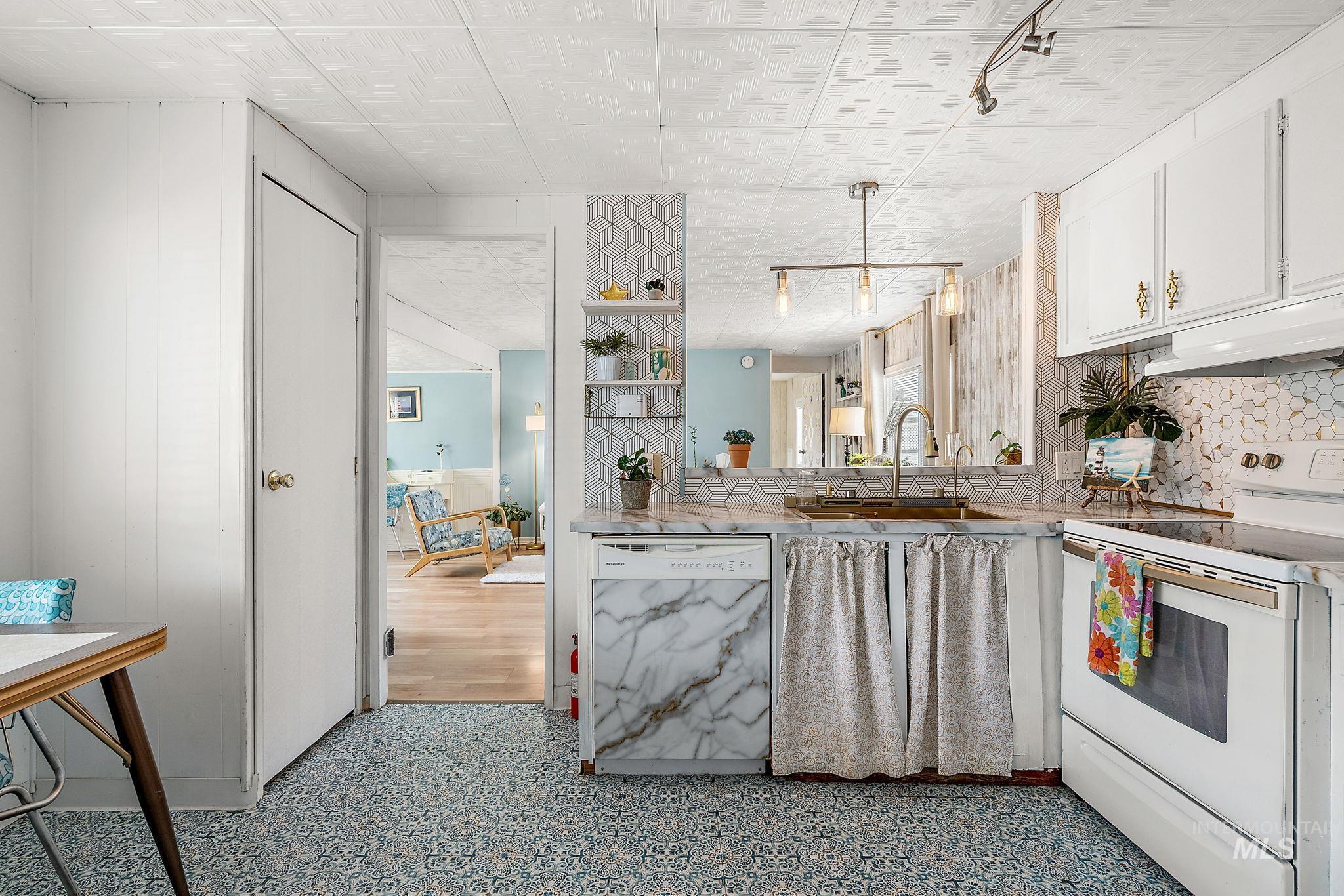 Kitchen with electric stove, dishwasher, under cabinet range hood, hanging light fixtures, and white cabinetry