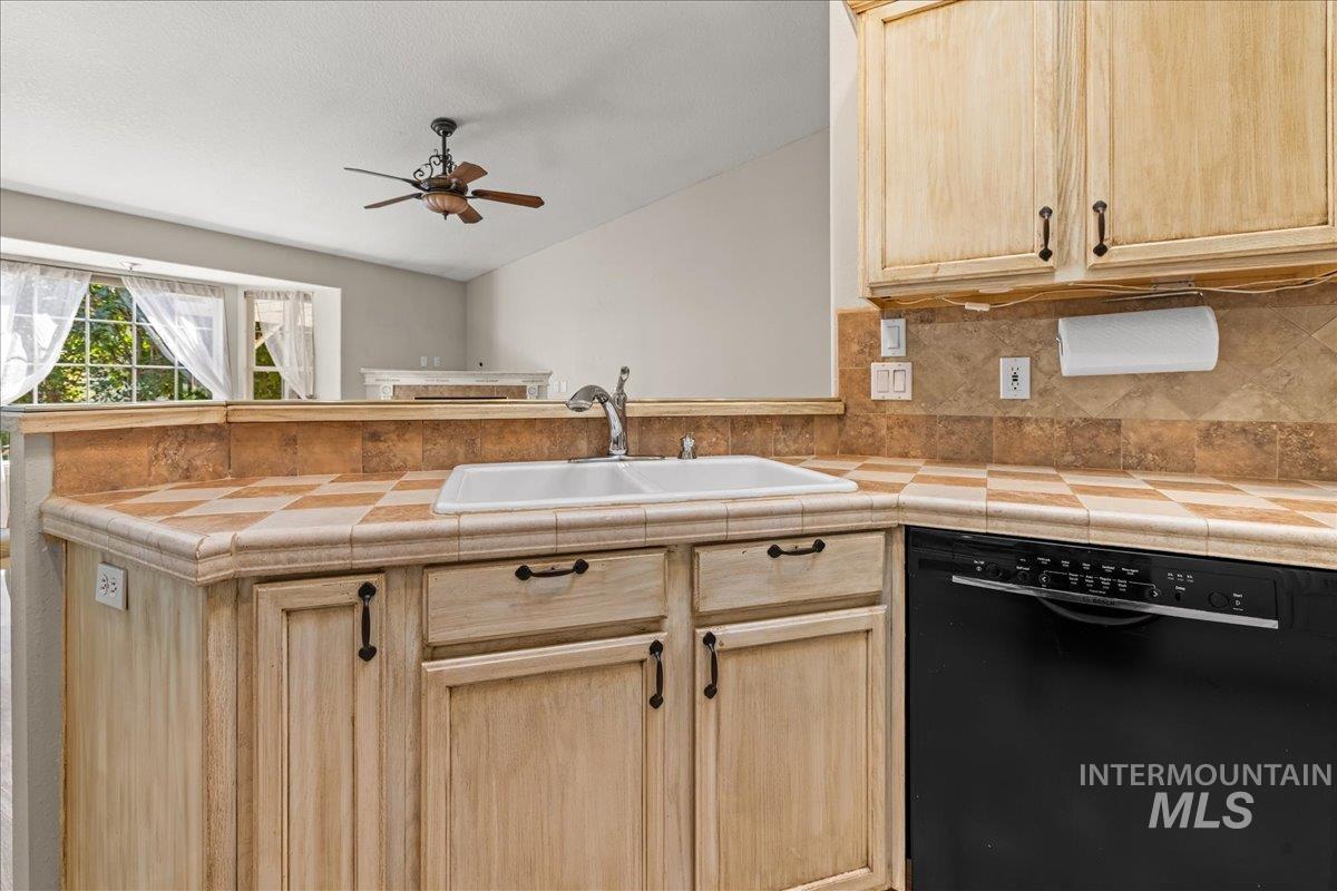 Kitchen with light brown cabinetry, dishwasher, tile counters, a peninsula, and tasteful backsplash