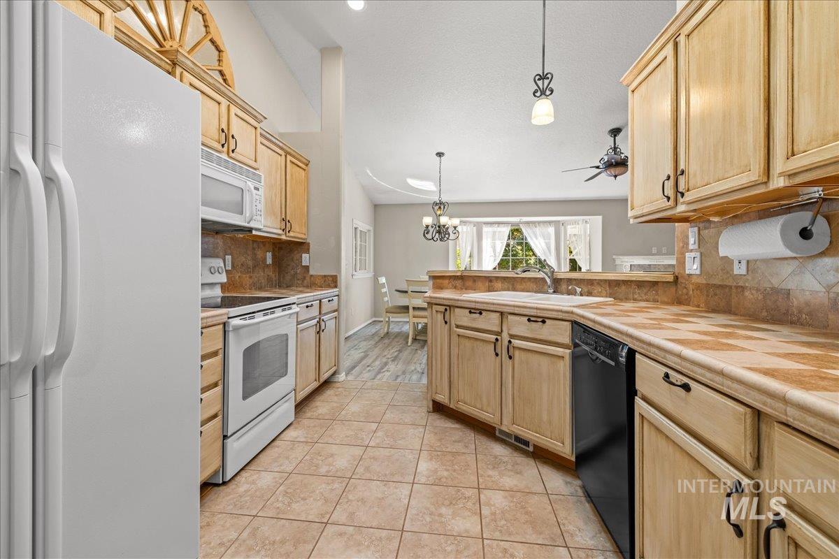 Kitchen featuring decorative backsplash, white appliances, a peninsula, light brown cabinetry, and hanging light fixtures