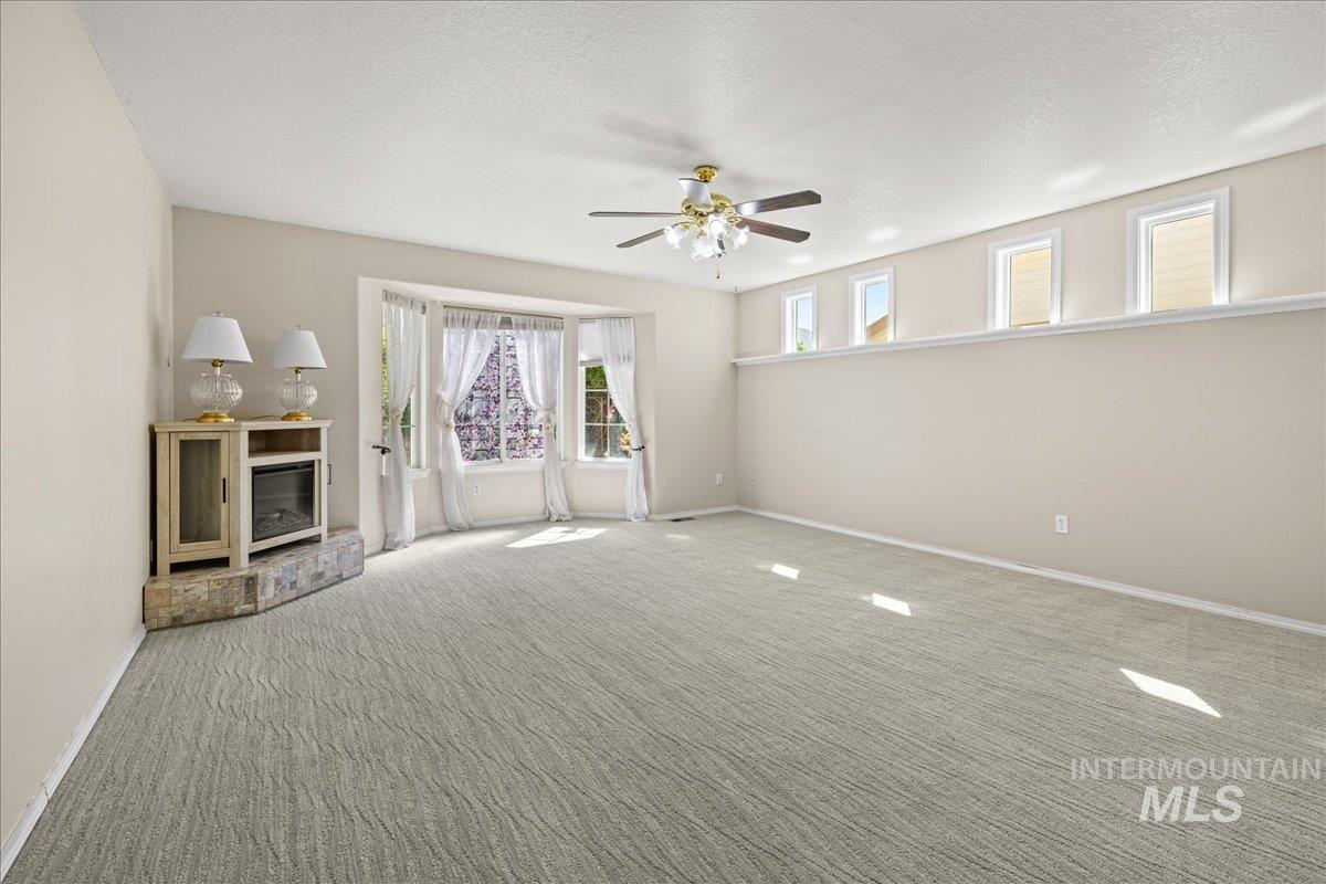 Unfurnished living room featuring carpet flooring, a ceiling fan, and a textured ceiling