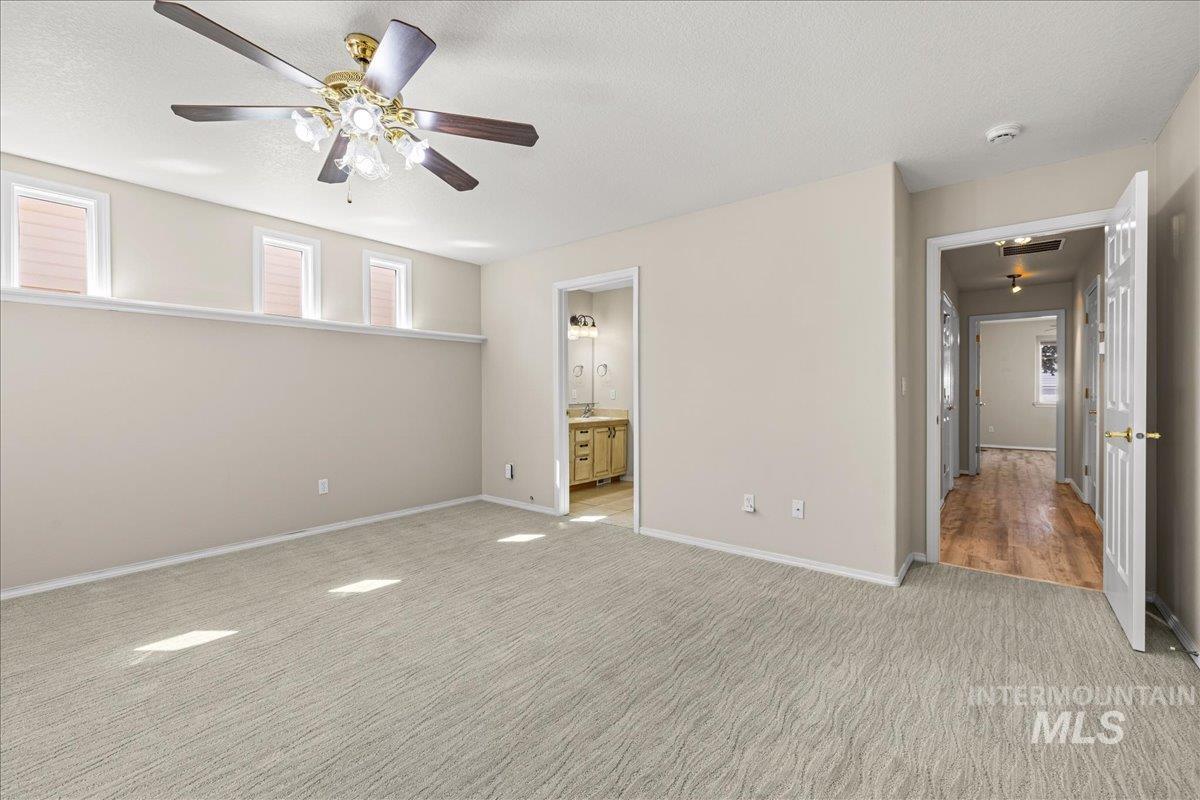 Unfurnished bedroom featuring light carpet, a textured ceiling, a ceiling fan, and connected bathroom