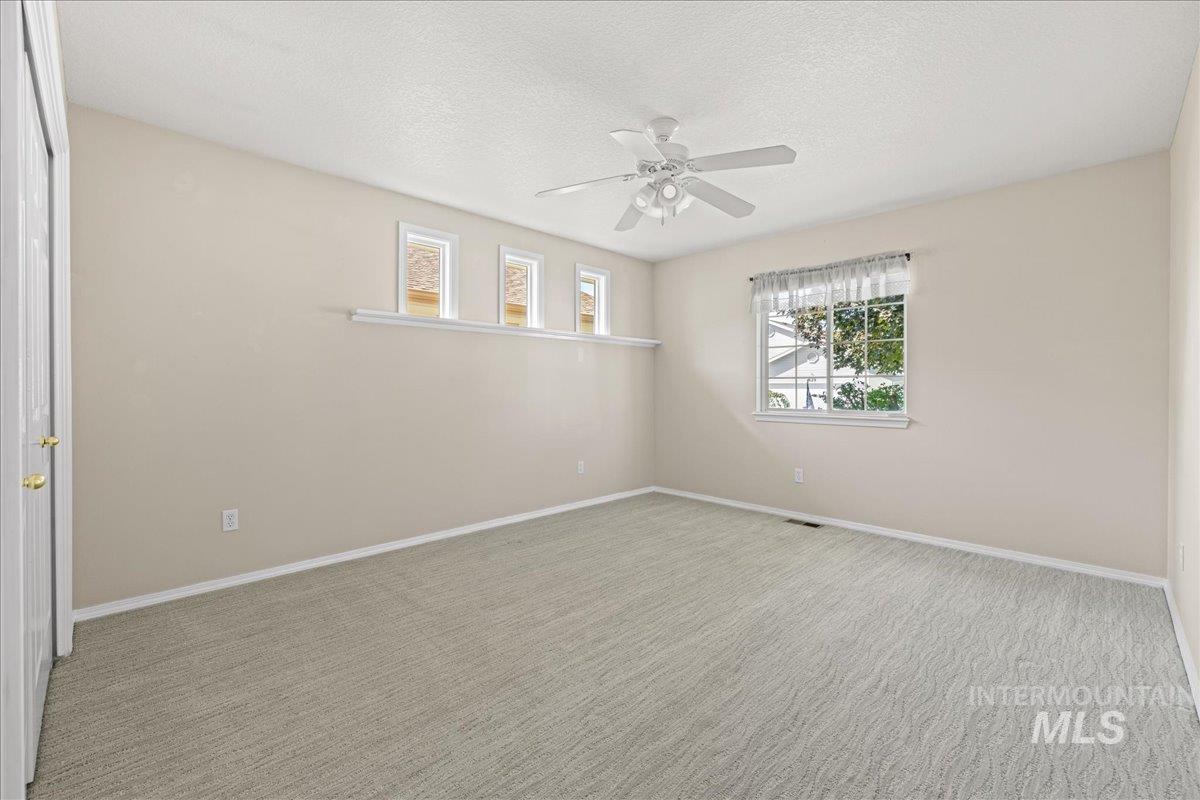 Empty room featuring carpet, a textured ceiling, and ceiling fan