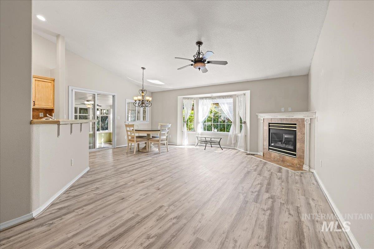 Unfurnished living room featuring light wood finished floors, ceiling fan, a fireplace, vaulted ceiling, and a chandelier