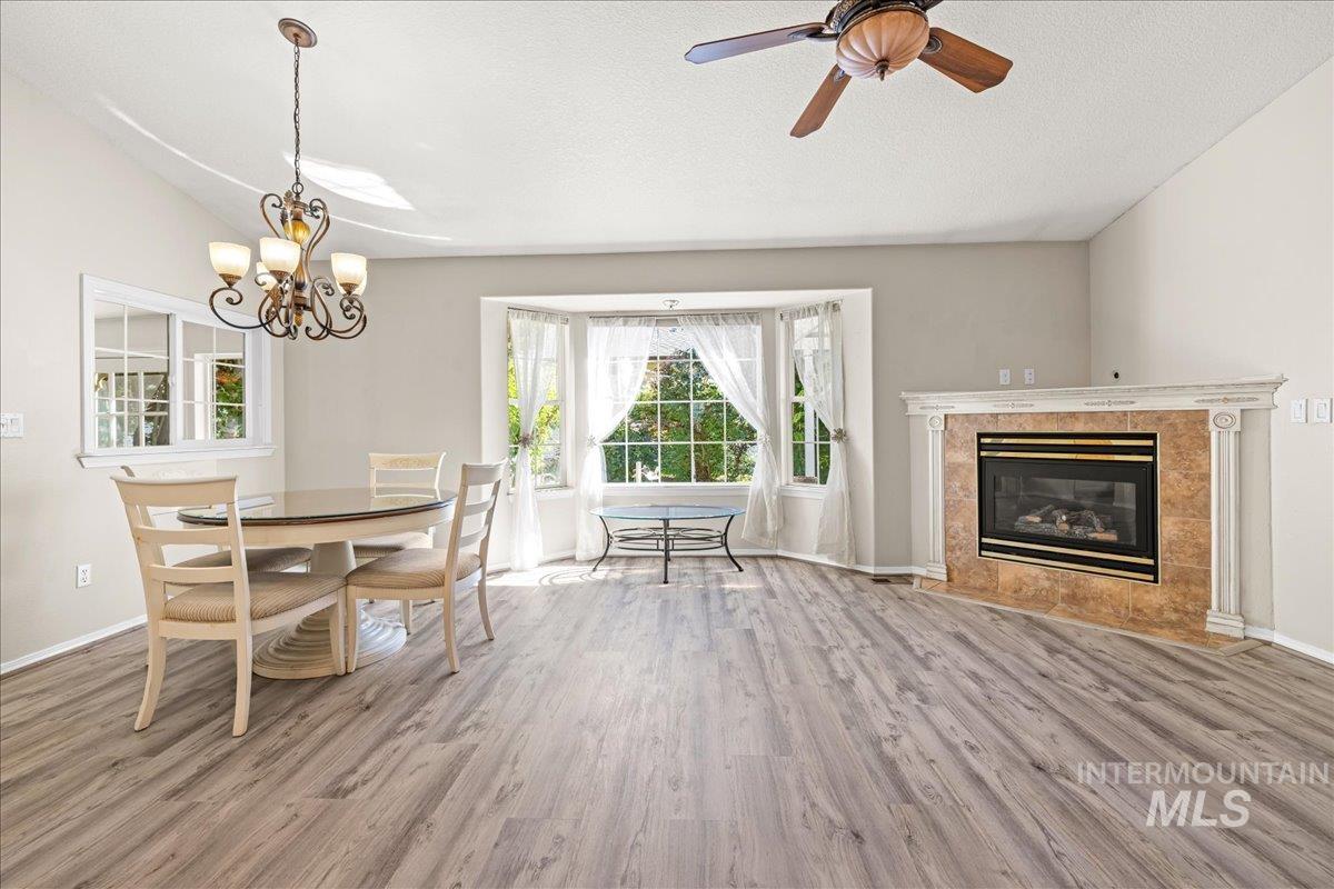 Dining space featuring light wood-type flooring, a tiled fireplace, a textured ceiling, and a ceiling fan