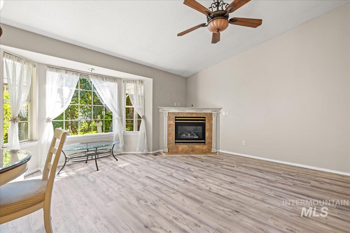 Living room with vaulted ceiling, wood finished floors, a textured ceiling, a premium fireplace, and ceiling fan
