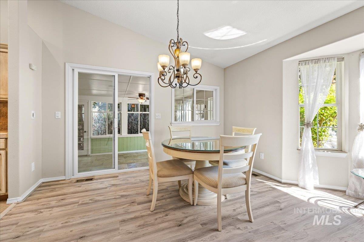 Dining area featuring lofted ceiling, plenty of natural light, light wood-style floors, and a chandelier