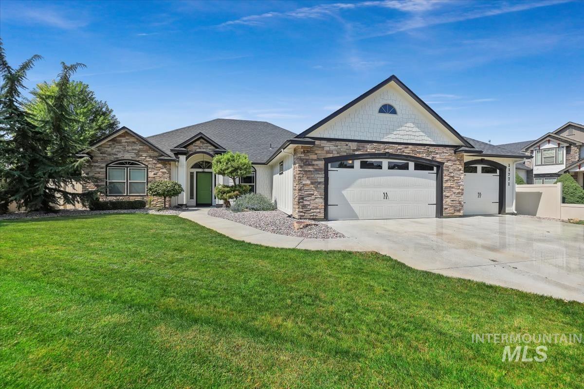 View of front of property with stone siding, a garage, driveway, and a front lawn