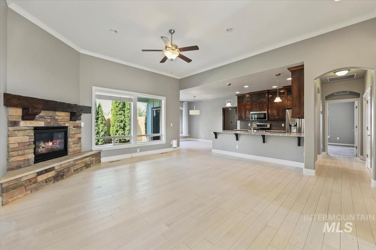 Unfurnished living room with arched walkways, a ceiling fan, crown molding, a fireplace, and light wood finished floors