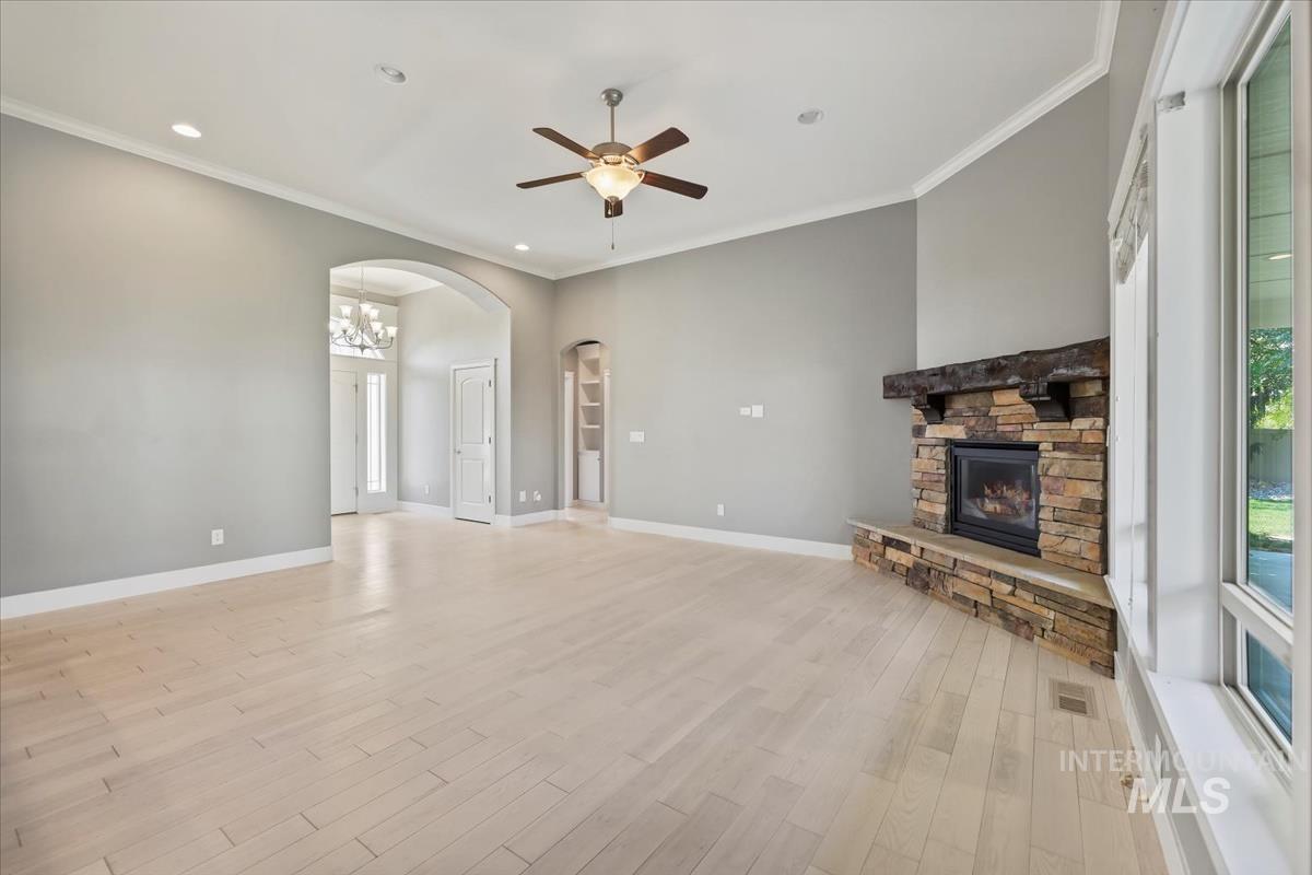Unfurnished living room featuring crown molding, recessed lighting, light wood-type flooring, a fireplace, and arched walkways