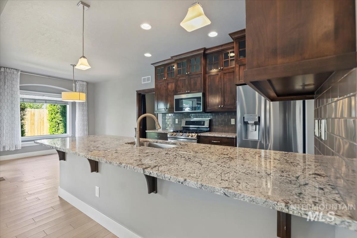 Kitchen featuring decorative light fixtures, tasteful backsplash, dark brown cabinets, glass insert cabinets, and a kitchen bar