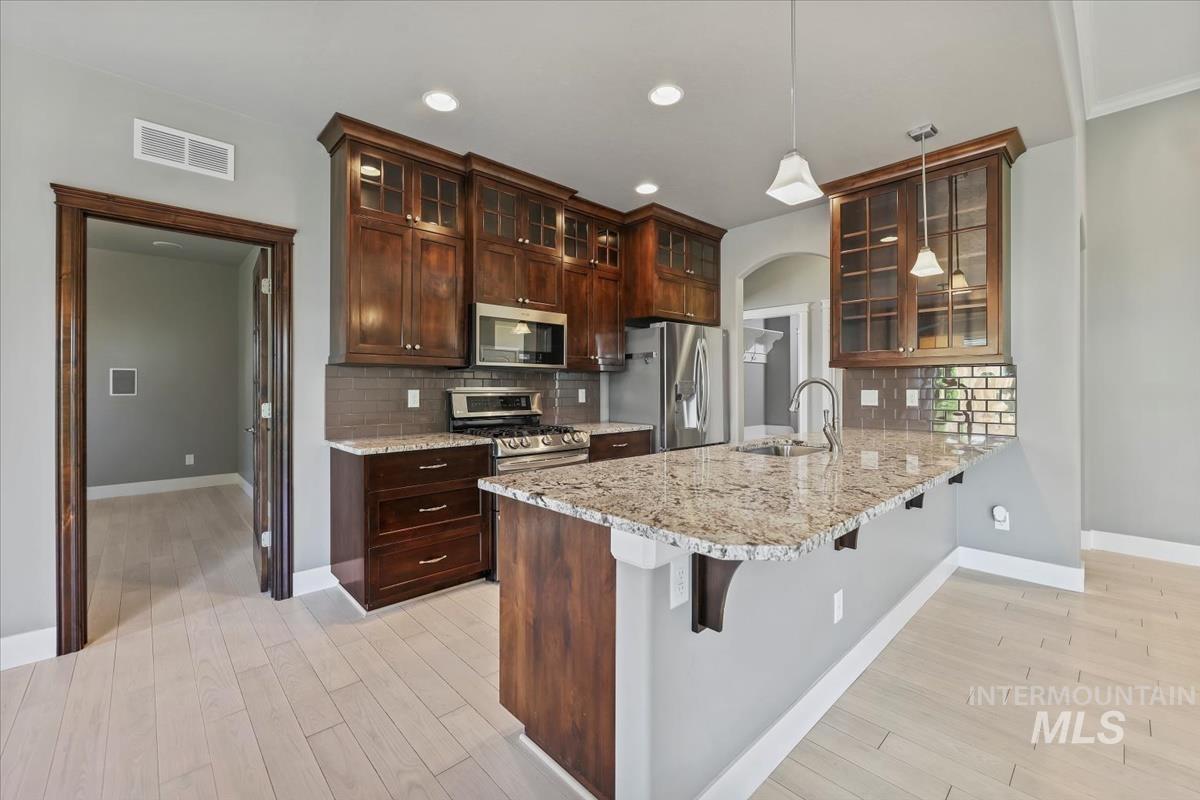 Kitchen featuring glass insert cabinets, tasteful backsplash, a breakfast bar area, light stone counters, and recessed lighting