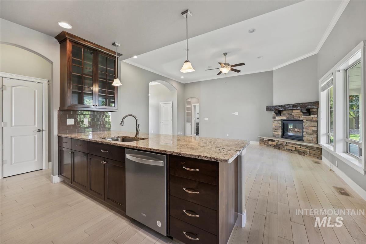 Kitchen with dark brown cabinets, pendant lighting, decorative backsplash, glass insert cabinets, and arched walkways