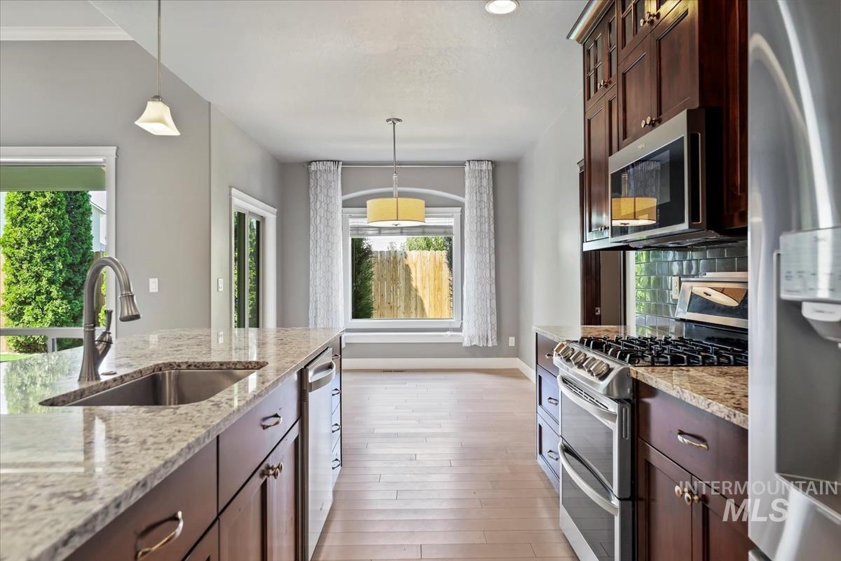 Kitchen featuring appliances with stainless steel finishes, pendant lighting, light stone counters, dark brown cabinetry, and light wood-style flooring