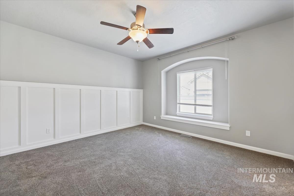 Master bedroom featuring a decorative wall, carpet floors, ceiling fan, and wainscoting