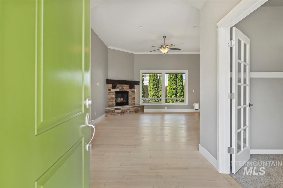 Entryway with crown molding, light wood finished floors, a stone fireplace, and a ceiling fan