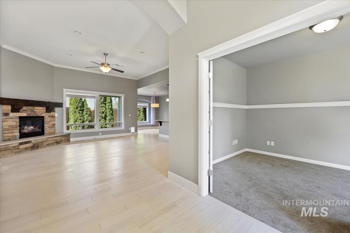 Unfurnished living room with ornamental molding, a stone fireplace, ceiling fan, light wood-style floors, and light carpet