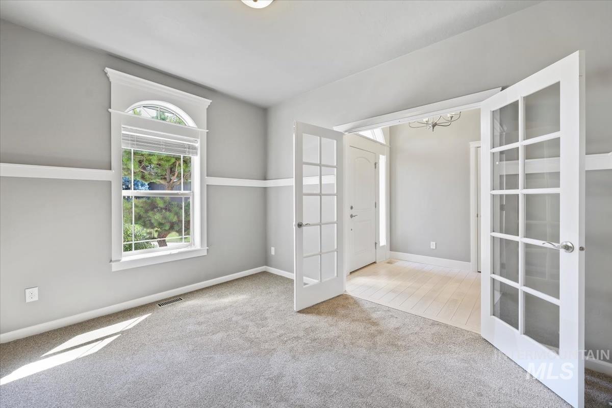 Carpeted spare room featuring french doors and a chandelier