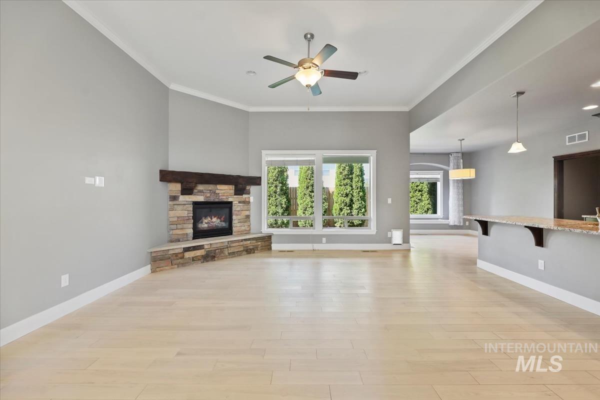 Unfurnished living room with ornamental molding, light wood-style floors, a stone fireplace, ceiling fan, and recessed lighting