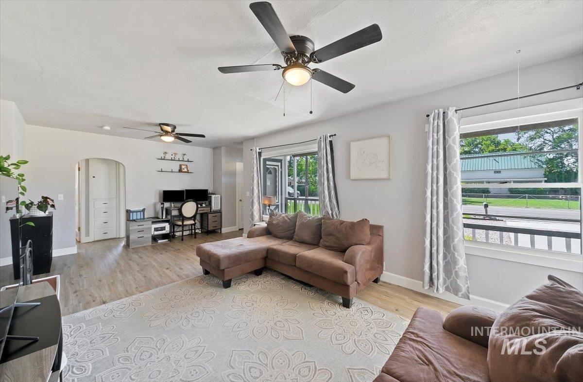 Living area with arched walkways, light wood-type flooring, a desk, and a ceiling fan