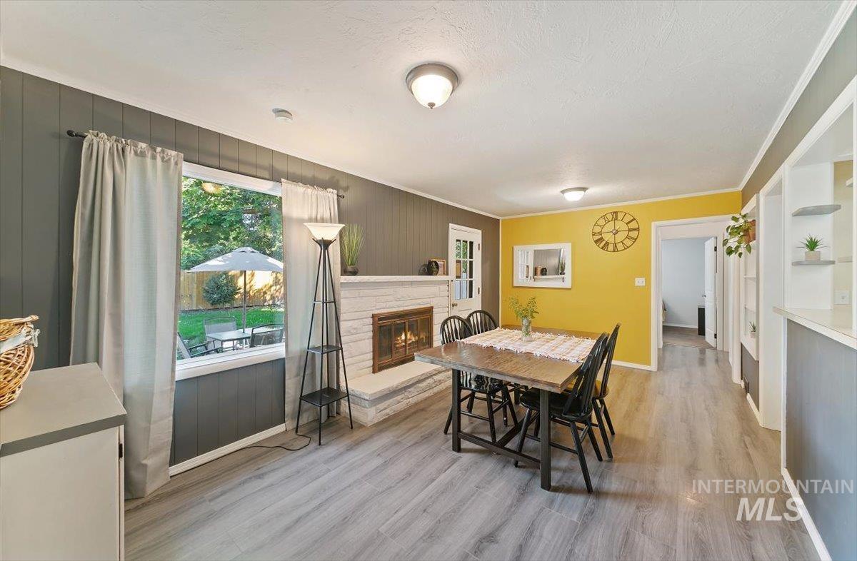 Dining area featuring light wood-style floors, crown molding, a stone fireplace, and a textured ceiling