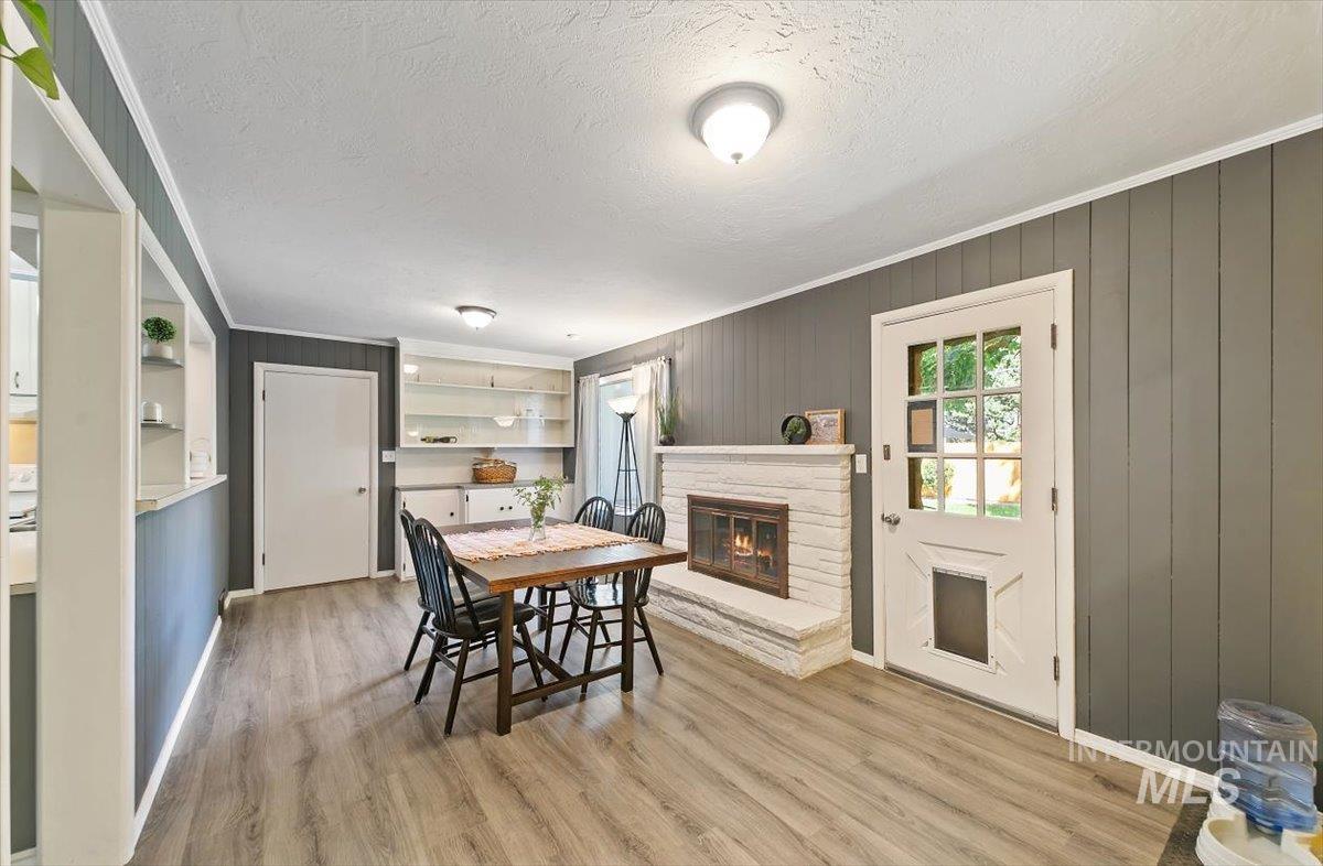 Dining space with light wood-type flooring, crown molding, wooden walls, a stone fireplace, and a textured ceiling