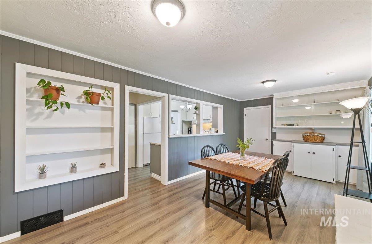 Dining area with built in features, crown molding, wood walls, light wood-type flooring, and a textured ceiling