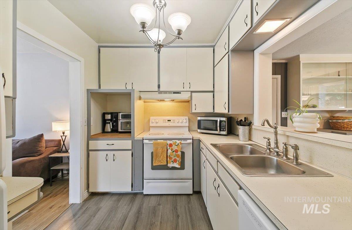 Kitchen featuring white appliances, light countertops, light wood-type flooring, and white cabinets