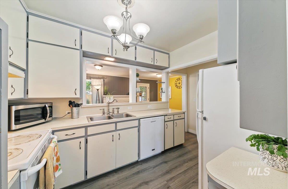 Kitchen featuring white cabinets, white appliances, light countertops, dark wood-style floors, and a chandelier