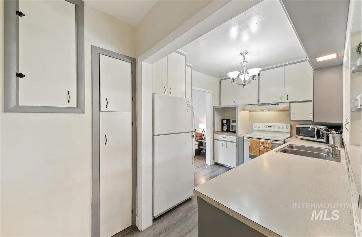 Kitchen with white appliances, light countertops, light wood-type flooring, a chandelier, and white cabinets