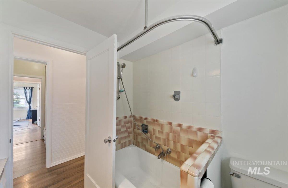 Full bathroom with tiled shower / bath combo, wood finished floors, and a wainscoted wall