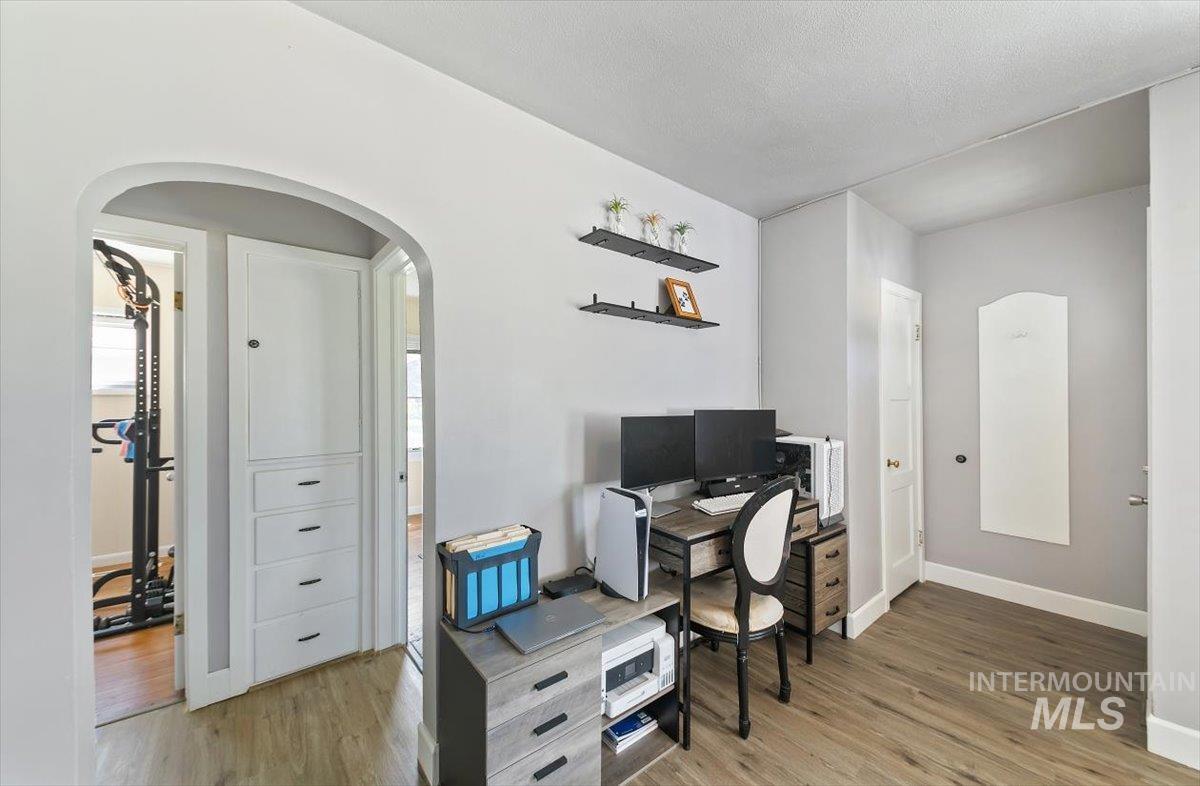 Home office featuring arched walkways, light wood-style floors, and a textured ceiling