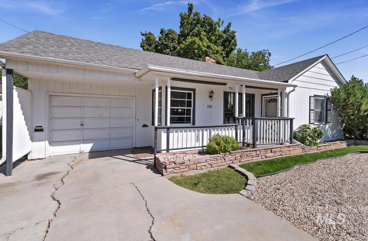 Single story home with a shingled roof, driveway, an attached garage, a porch, and a chimney