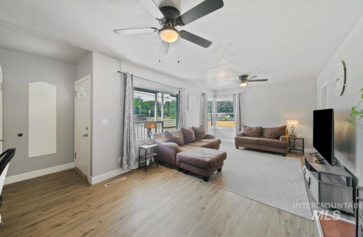 Living area with light wood-style floors, a textured ceiling, and ceiling fan