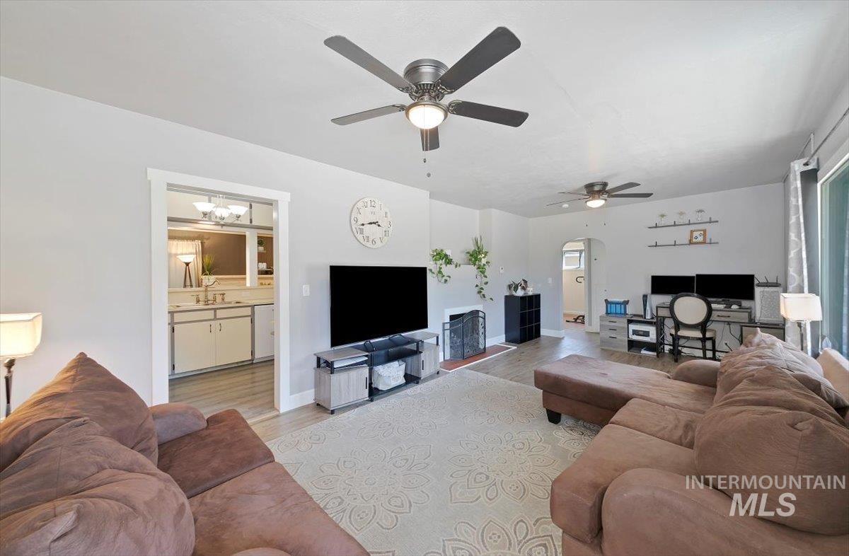 Living room with arched walkways, light wood-style flooring, and ceiling fan