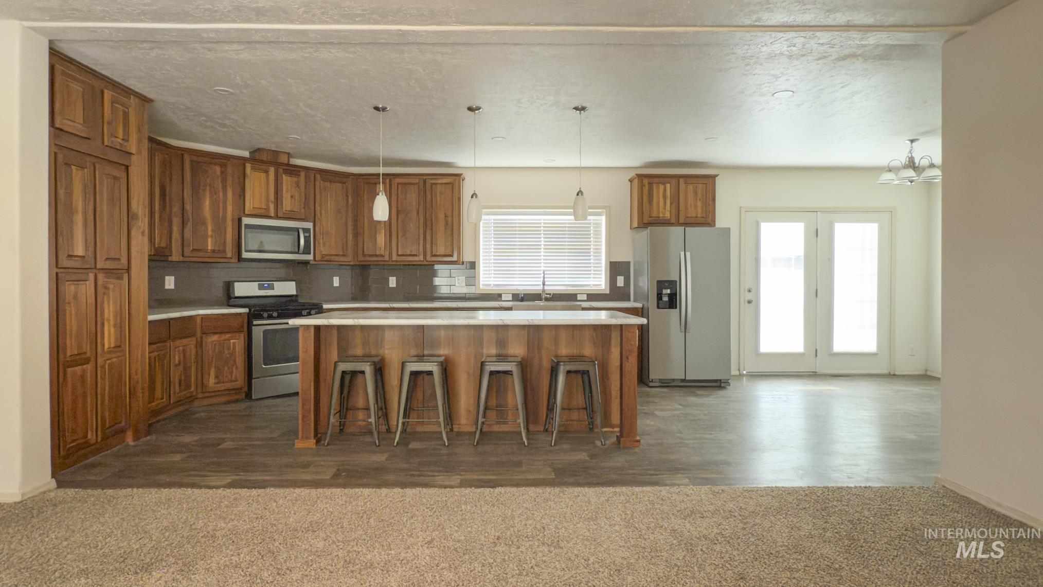 Kitchen featuring brown cabinets, decorative backsplash, appliances with stainless steel finishes, light countertops, and hanging light fixtures