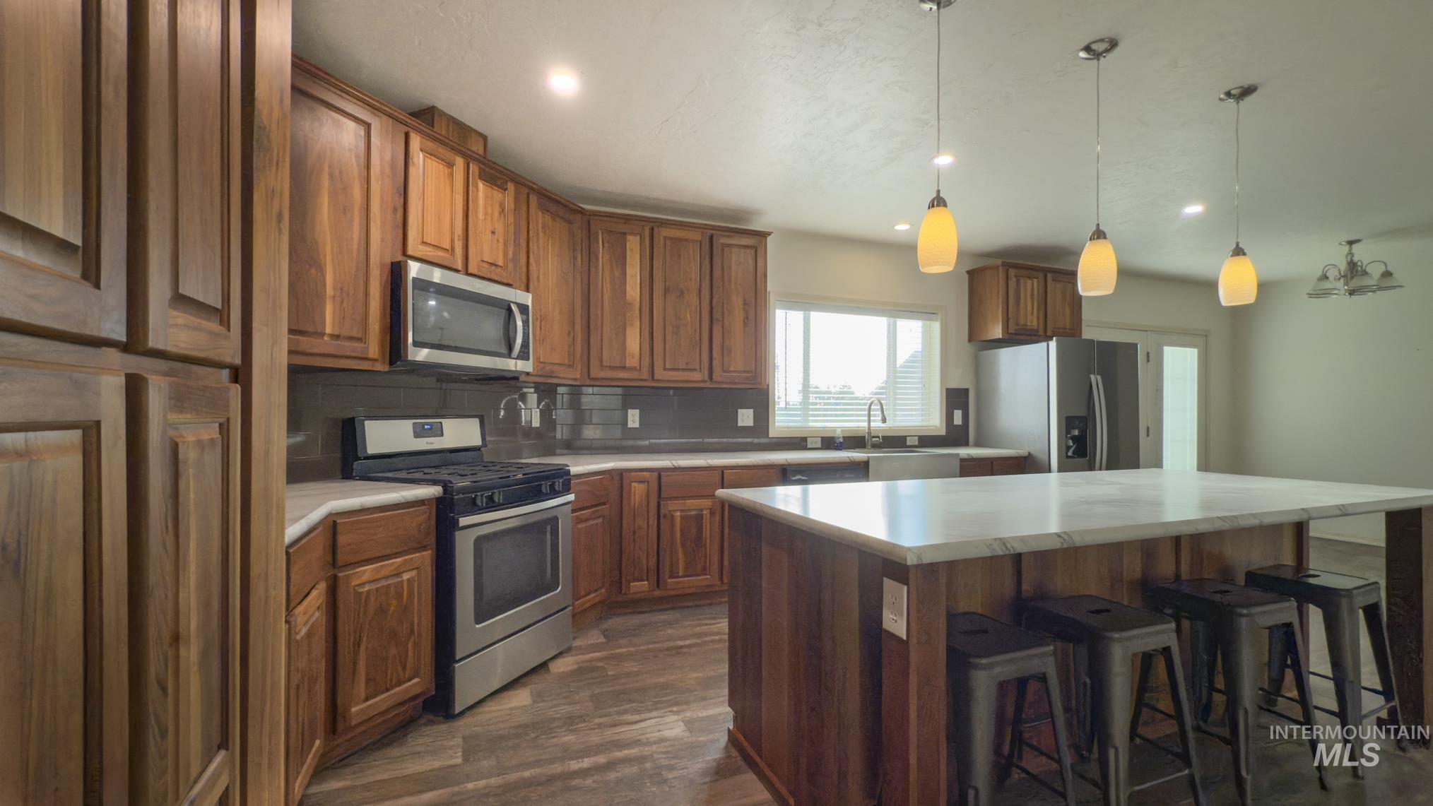 Kitchen featuring a kitchen bar, stainless steel appliances, tasteful backsplash, light countertops, and hanging light fixtures