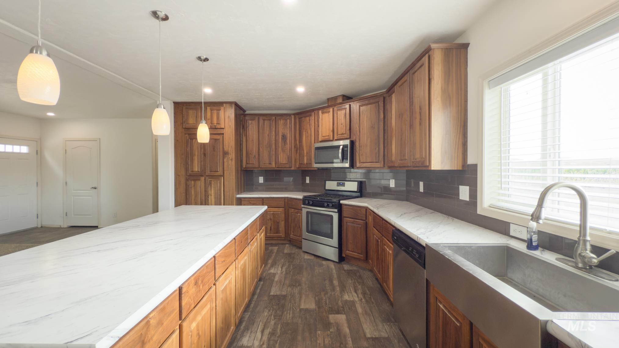 Kitchen featuring stainless steel appliances, brown cabinets, dark wood-style floors, tasteful backsplash, and hanging light fixtures