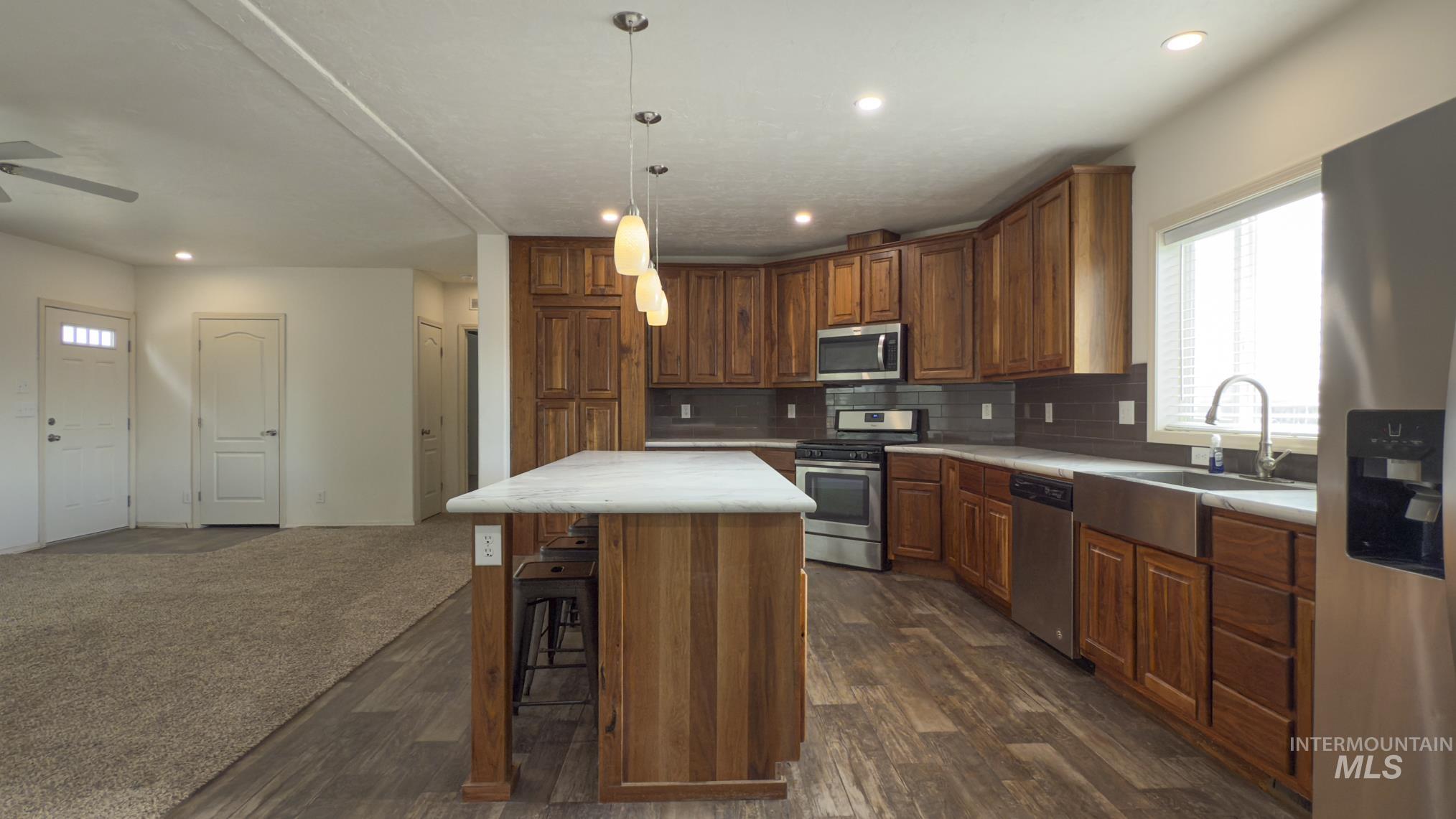 Kitchen with stainless steel appliances, a kitchen island, brown cabinets, light countertops, and a breakfast bar area